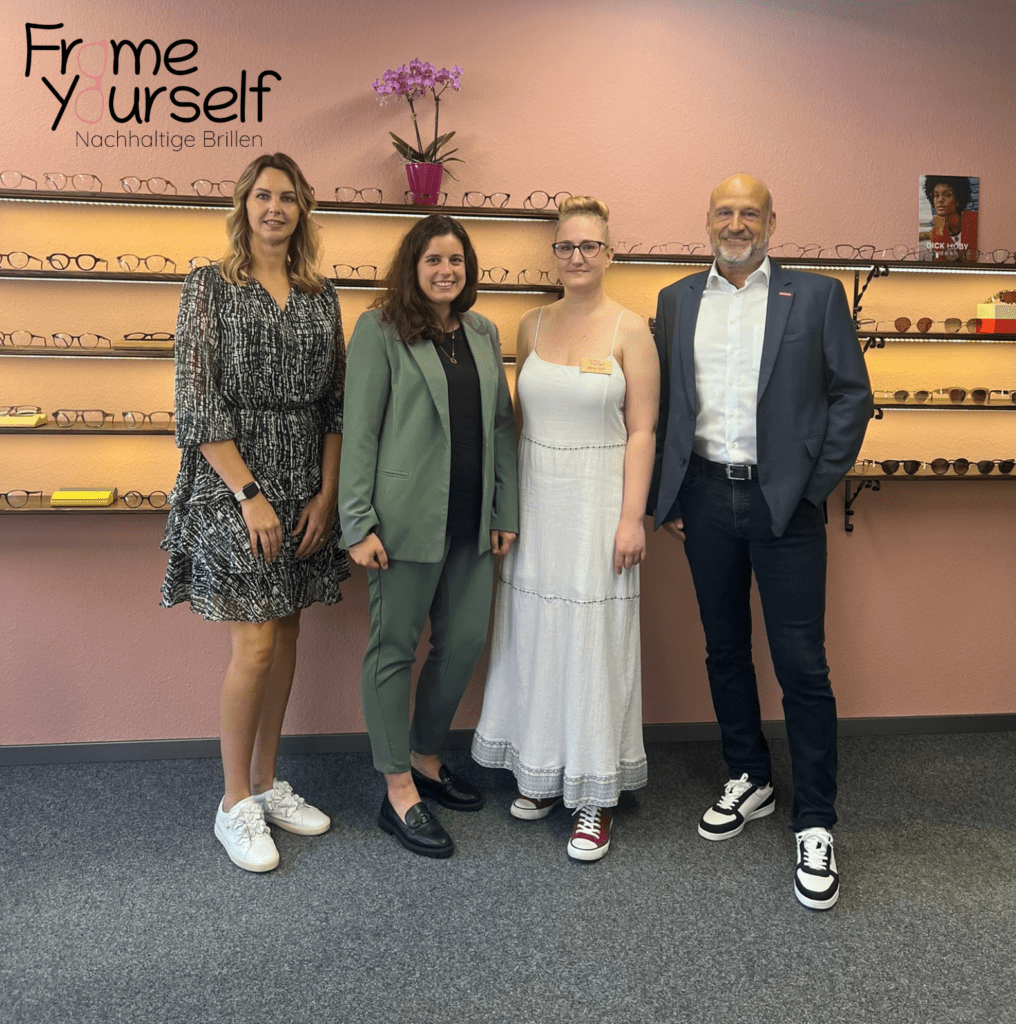 Christina Biehl (WFG BIR mbH), Chiara Mele (WFG BIR mbH), Anne Neil (FrameYourself) und Michael Fuhr (HWK Koblenz) stehen vor dem Brillenregal im Geschäftsraum von FrameYourself.